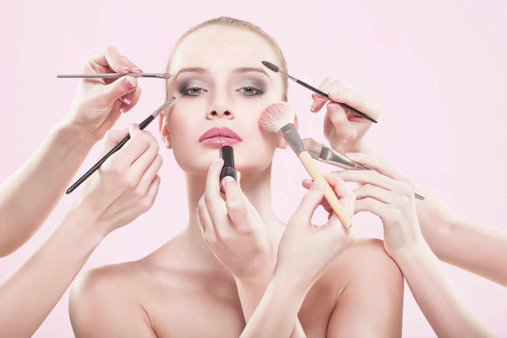 A woman having makeup applied by multiple hands.