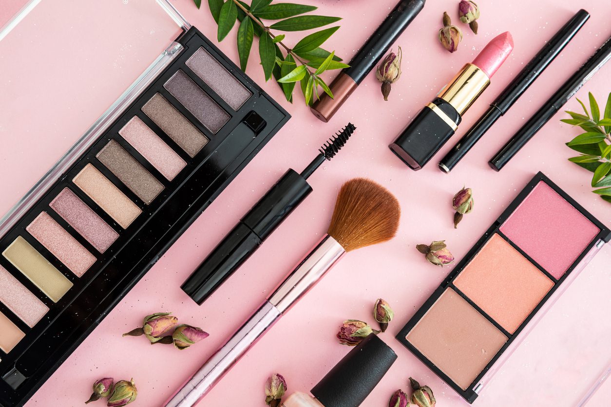 Flat lay of various makeup products arranged aesthetically on a pink surface.